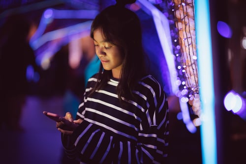 SMS Delivery Asian young girl using a mobile phone in downtown, Bokeh city light in background