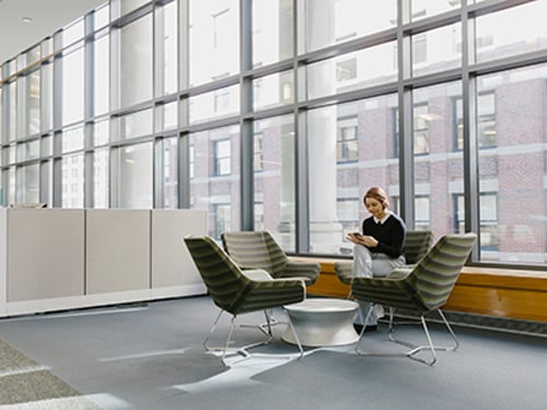 Hispanic Businesswoman Using Mobile Phone Alone In Office Lobby Team sitting around table doing work on laptops and smartphones using a Vonage integration