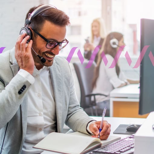 Call Queue Blog Thumbnail Photo of a smiling call center agent talking to a customer through his headset and writing notes